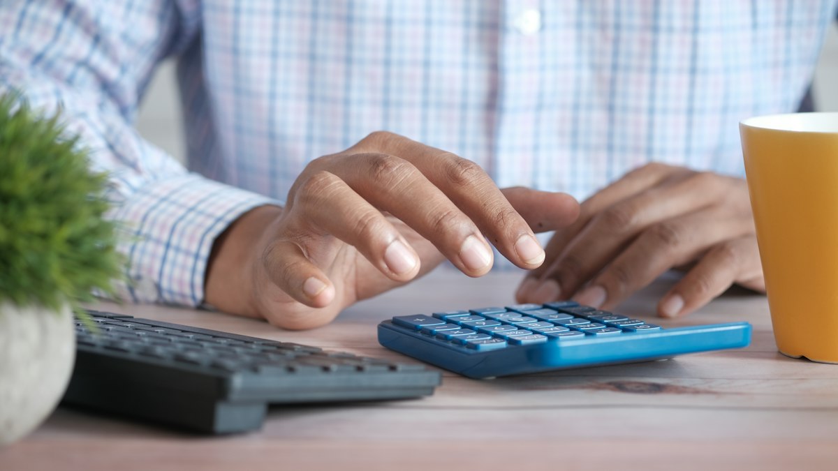 Mains d'un homme effectuant un calcul sur une calculatrice posée sur un bureau