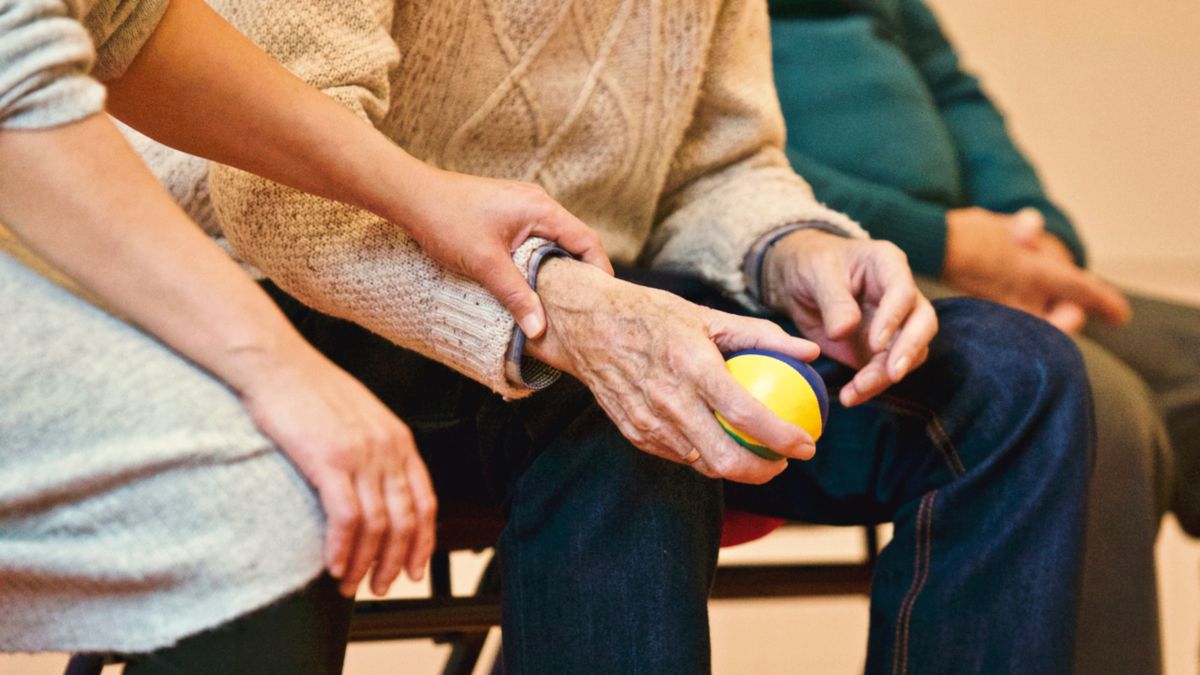 Main d'une aidante posée sur le bras d'une personne âgée qui tient une balle